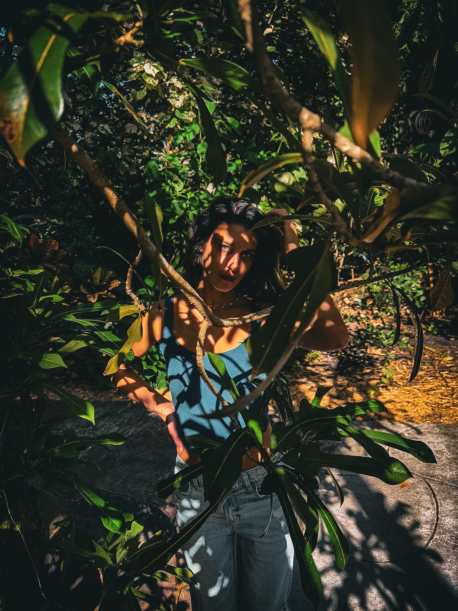 Eleanora among sunlit tropical foliage, dappled light falling across her face and shoulders