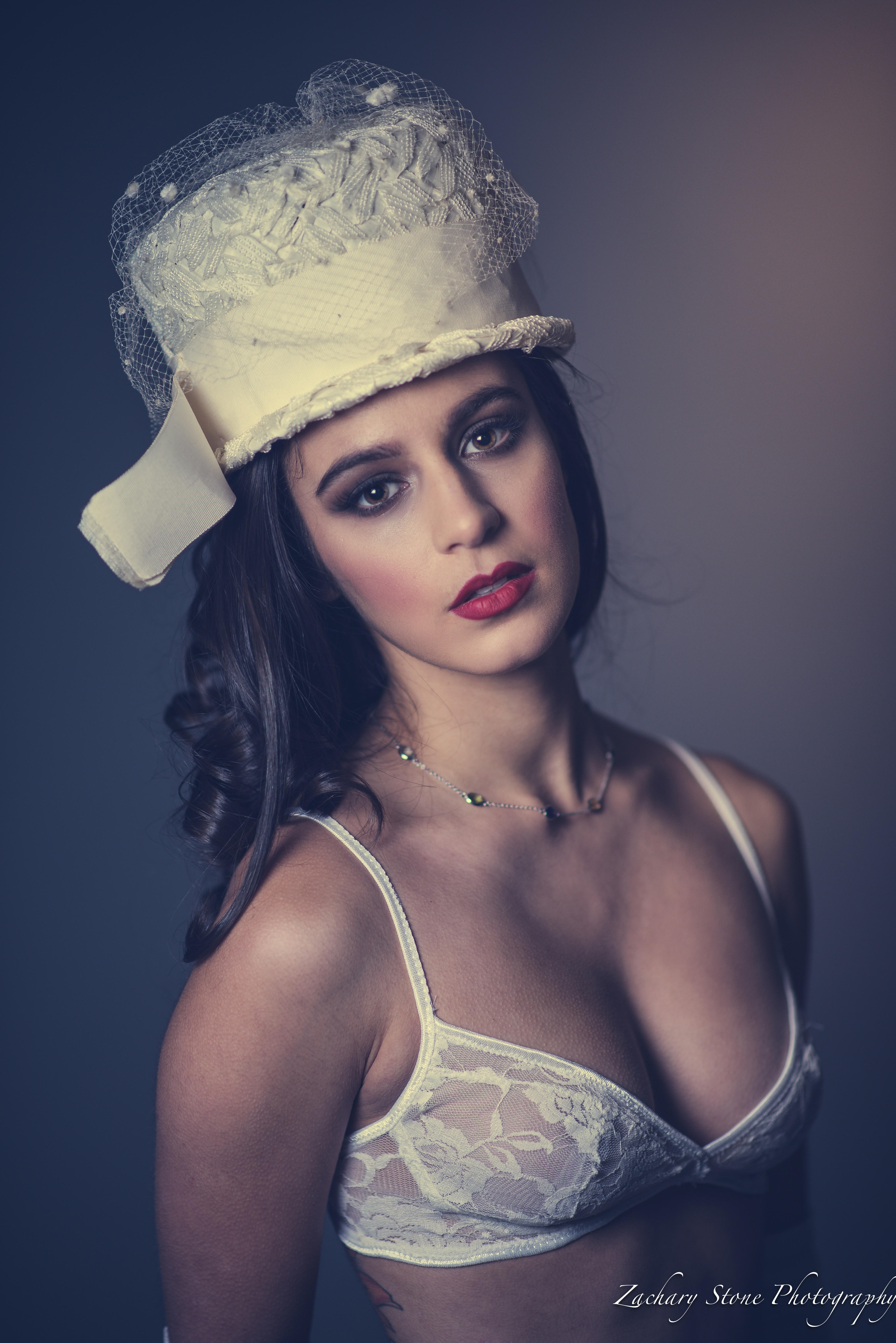 Eleanora in a delicate lace bralette and a wide-brimmed vintage hat, gazing steadily into the lens