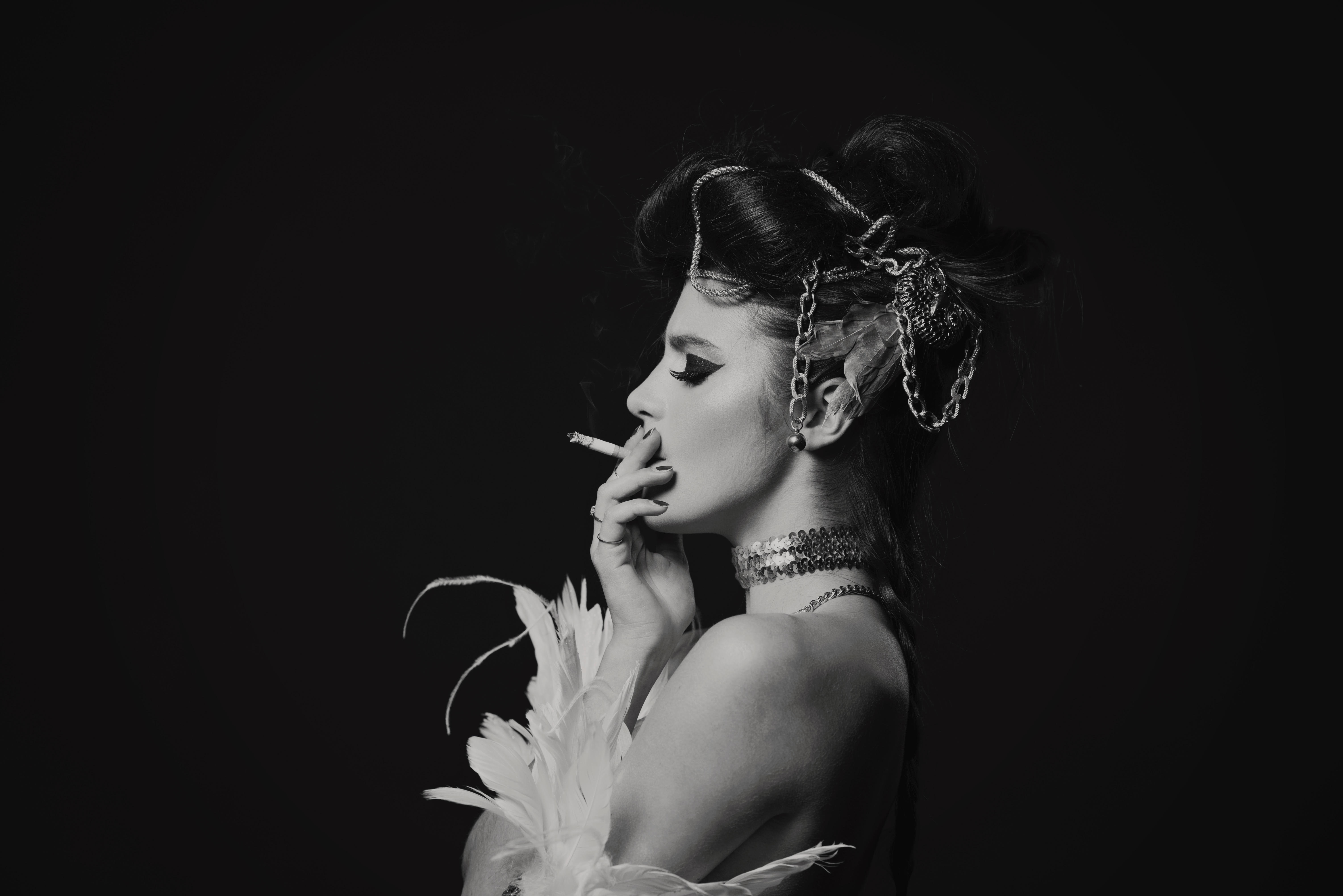 Black-and-white editorial portrait of Eleanora in profile, a feather at her shoulder and soft smoke curling past her face