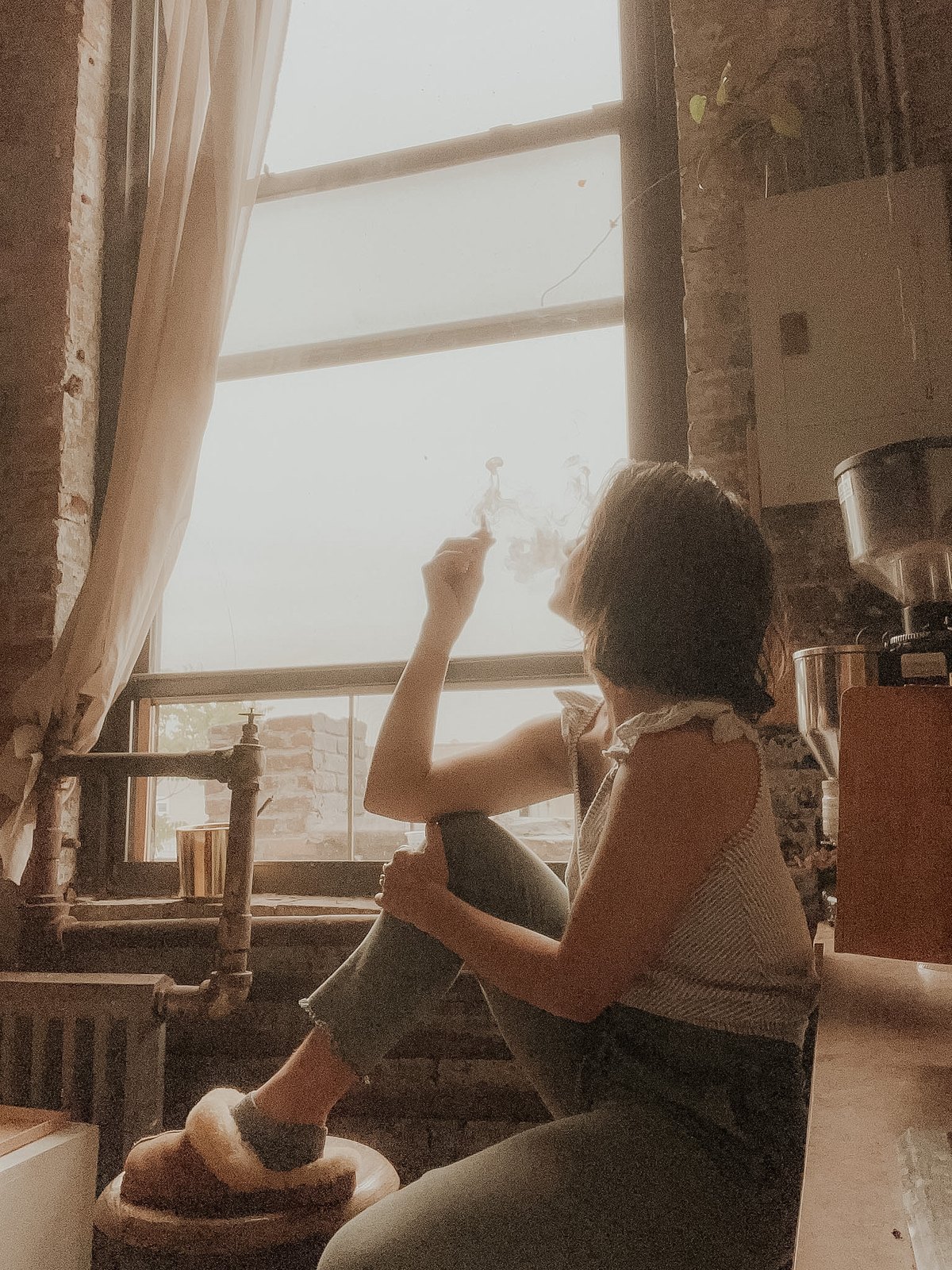 Eleanora at a loft window in the golden late light, cigarette smoke curling in the sun